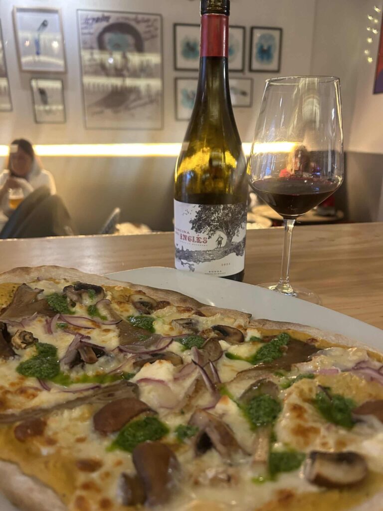 Vista de una pizza recién hecha super deliciosa junto a una botellita de vino tinto